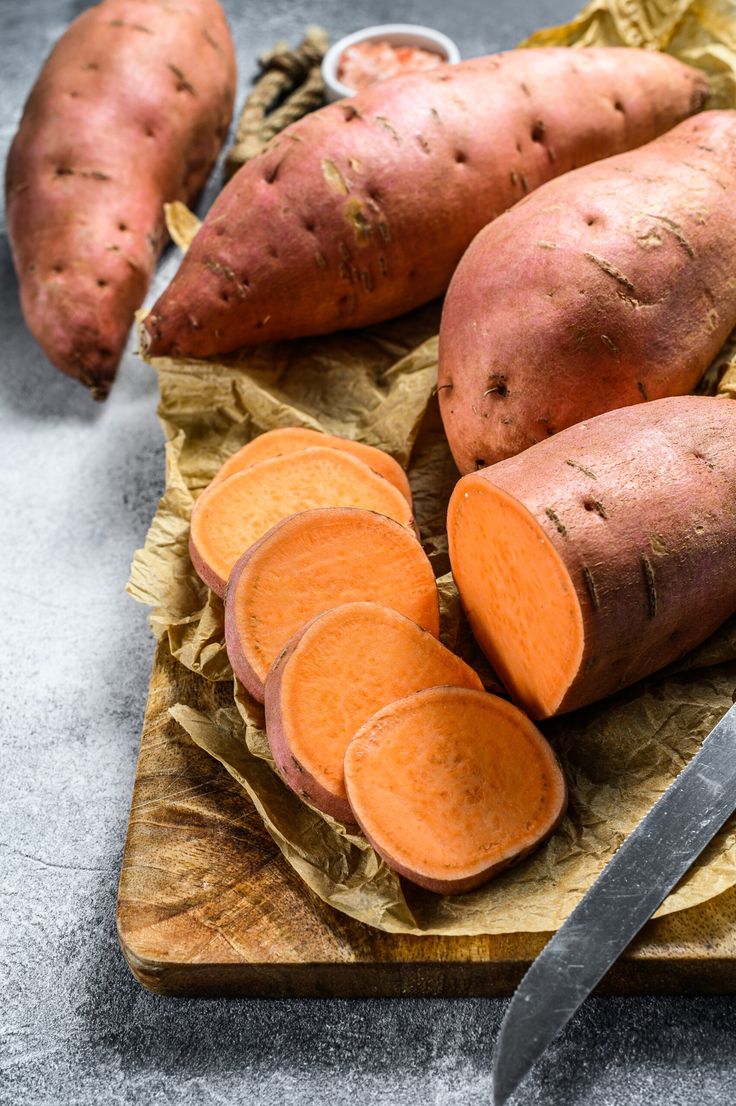 several sweet potatoes on a cutting board with a knife