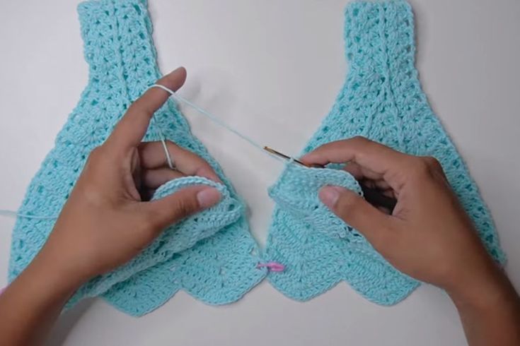 two hands are knitting the ends of a crocheted mitt with cotton yarn