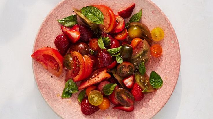 a pink plate topped with sliced strawberries and tomatoes