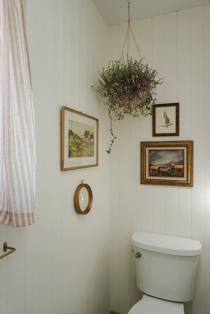 a white toilet sitting in a bathroom next to a painting and framed pictures on the wall