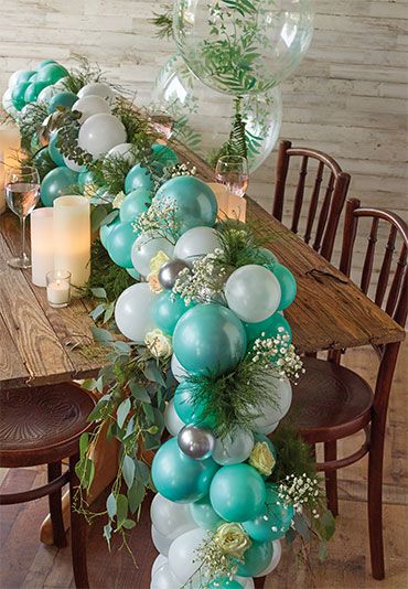 a long table with balloons and greenery on it