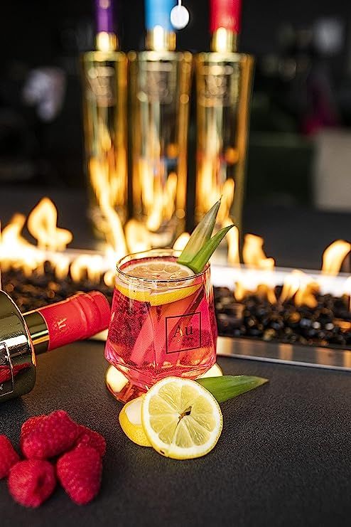 a glass filled with liquid next to some raspberries and lemons on a table