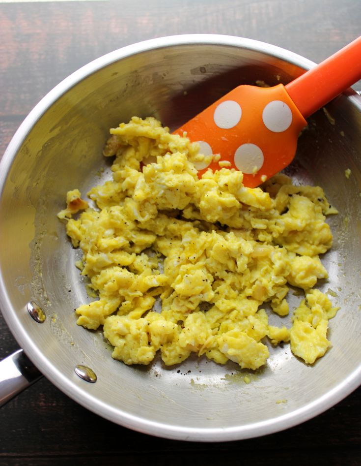 scrambled eggs in a metal bowl with an orange spatula