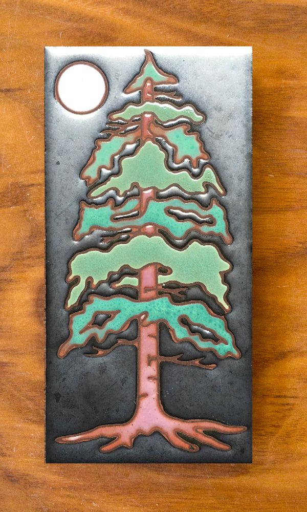 a metal plaque with a green and pink christmas tree on it's side, sitting on a wooden table