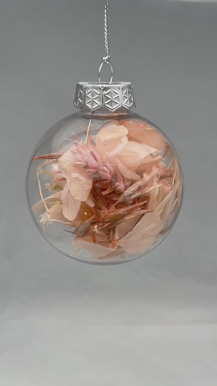 a glass ball ornament with flowers in it hanging from a chain on a gray background