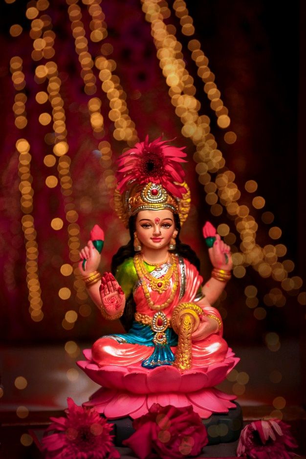 a statue of the hindu god sitting on top of a pink flowered platform with lights in the background