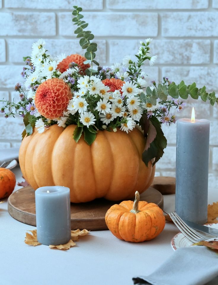 an arrangement of flowers in a pumpkin shaped vase on a table with candles and napkins