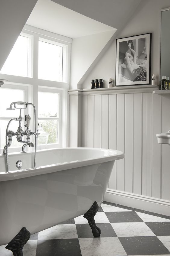 a white bath tub sitting under a window next to a checkerboard tile floor