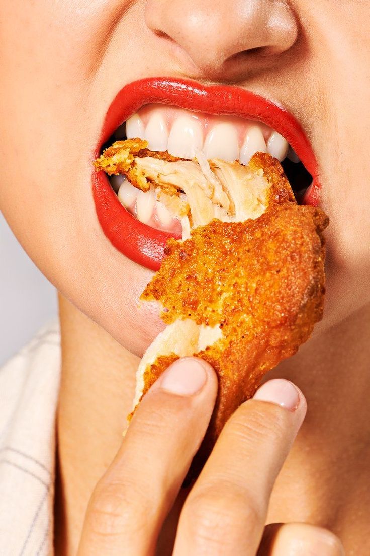 a woman biting into some food with her mouth open and red lipstick on the lips