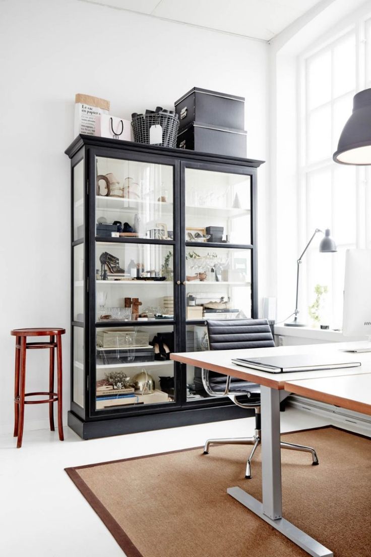 a black cabinet with glass doors and shelves in an office space, next to a computer desk