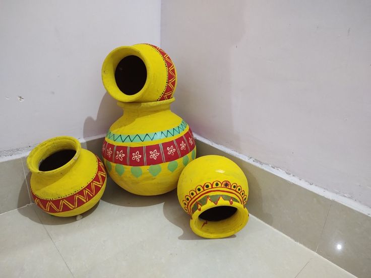 three yellow vases sitting next to each other on the floor in front of a wall