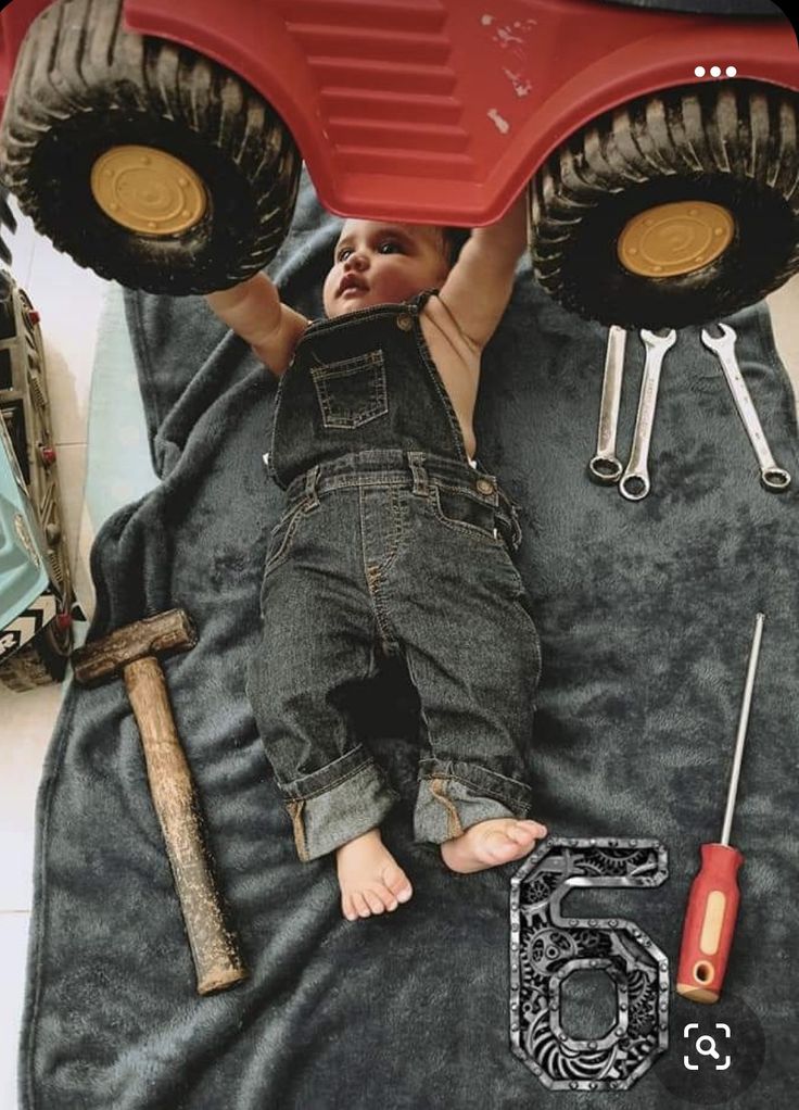 a baby laying on top of a giant red monster truck with lots of tools around it