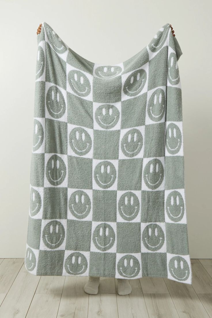 a gray and white blanket with smiley faces on it, hanging from the side of a wooden floor