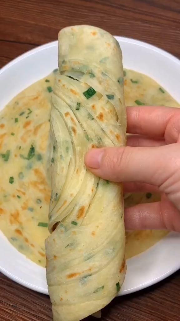 a person is holding up some food on a white plate with green onions and cheese