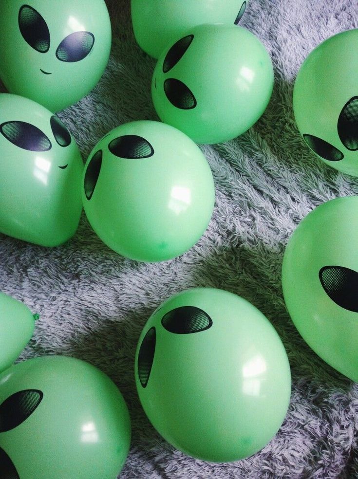 many green balloons with black eyes and nose designs on them are laying on a gray blanket