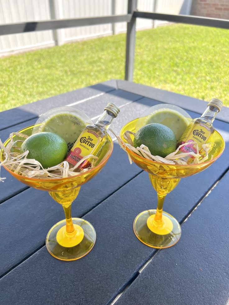 two yellow wine glasses filled with fruit on top of a wooden table next to each other