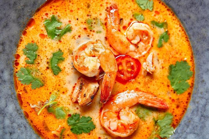 a bowl of soup with shrimp, tomatoes and cilantro on the side as garnish