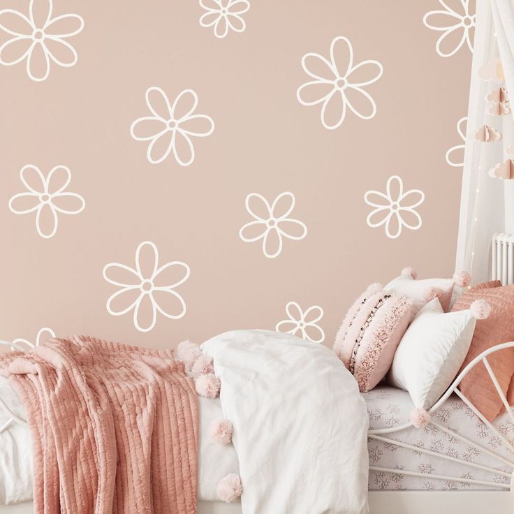 a white bed sitting next to a pink wall with flowers on the walls and pillows