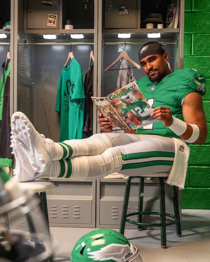 a man sitting in a locker reading a football news paper with his feet propped up on a stool