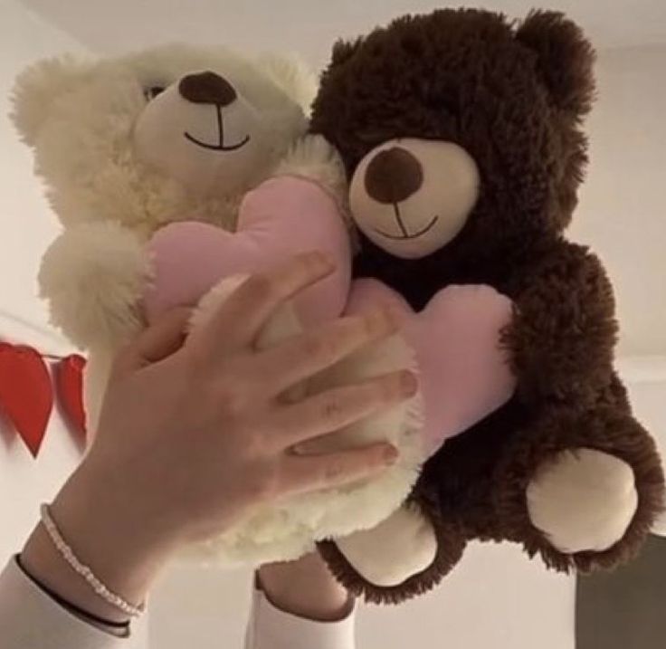 a person holding two teddy bears in their hands with hearts hanging from the ceiling behind them