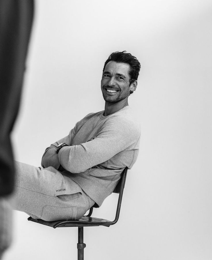 a smiling man sitting on top of a chair next to a person with his legs crossed