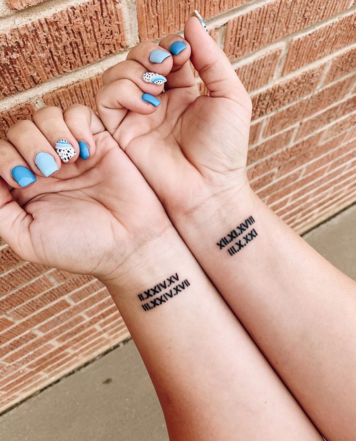 two people with matching tattoos on their arms holding each other's hands in front of a brick wall