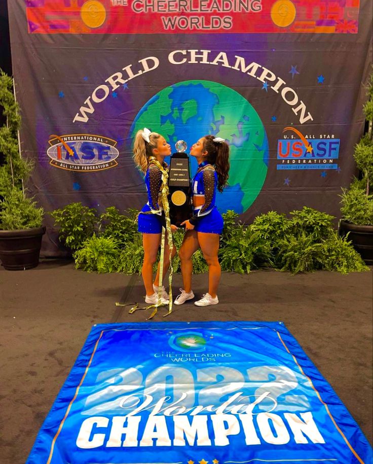 two cheerleaders stand on the stage with their trophy