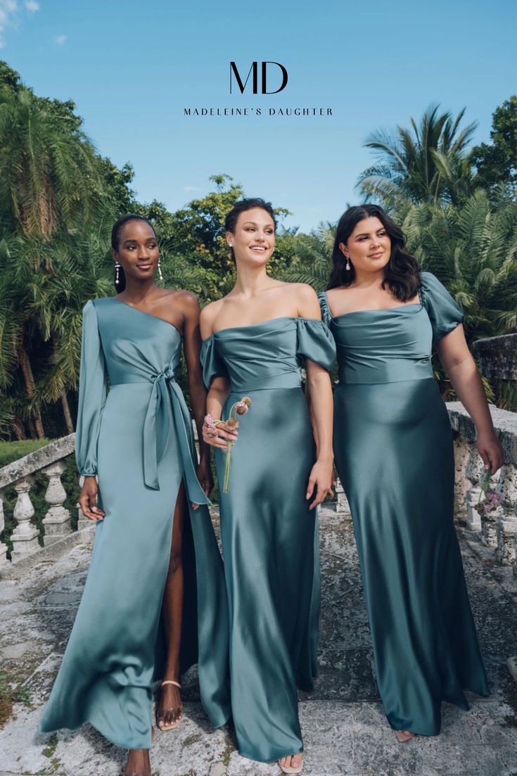 three women in long dresses posing for the camera with palm trees and blue sky behind them