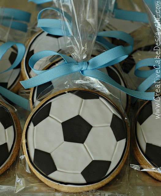 decorated cookies in the shape of soccer balls tied with blue ribbon and plastic wrappers