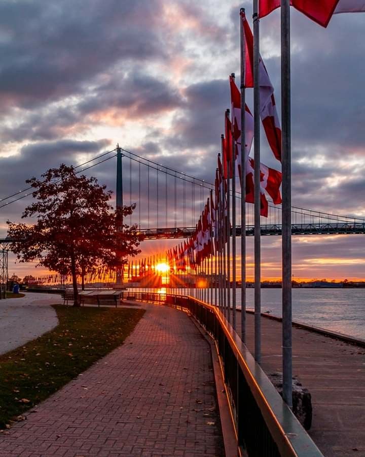 the sun is setting behind some flags on the side of the road by the water