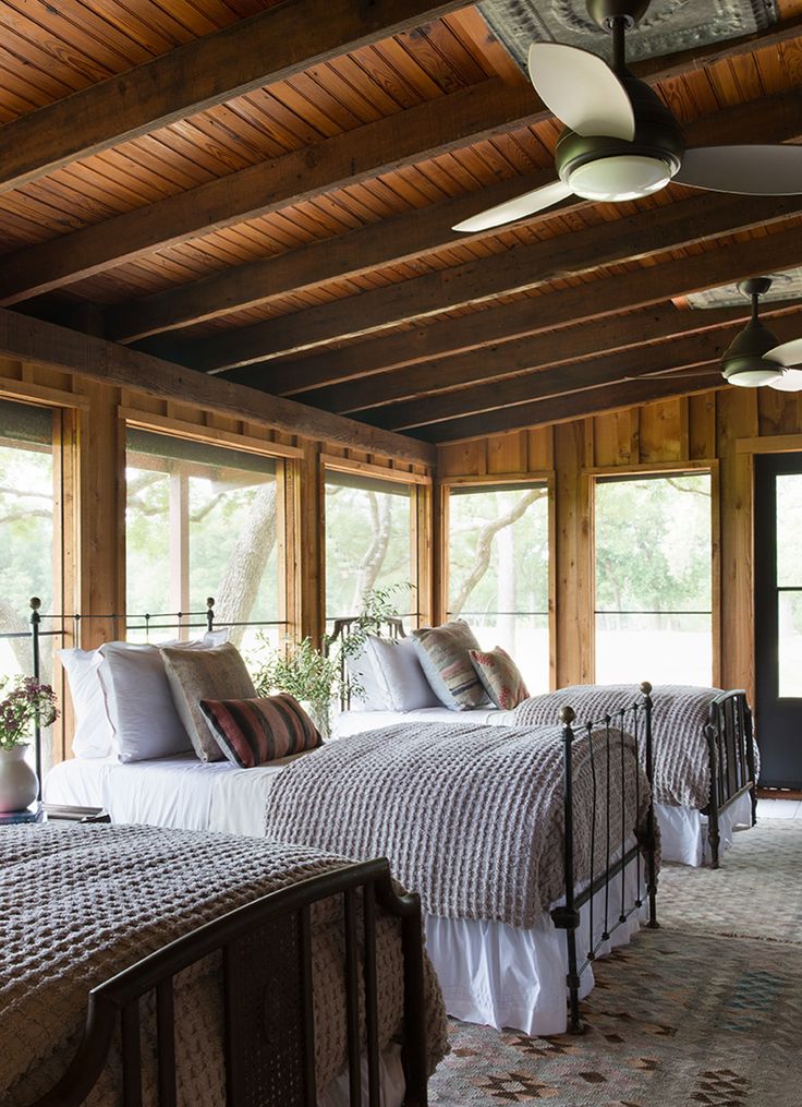 two beds in a room with wooden ceiling and windows