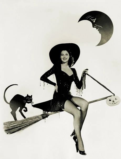 a black and white photo of a woman in a witch costume with a cat on her back