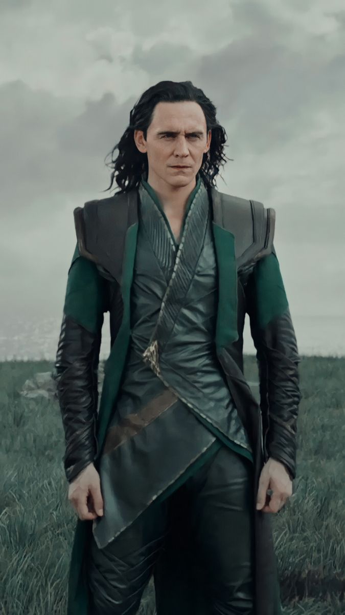 a man dressed in green and black standing on top of a grass covered field with his hands in his pockets