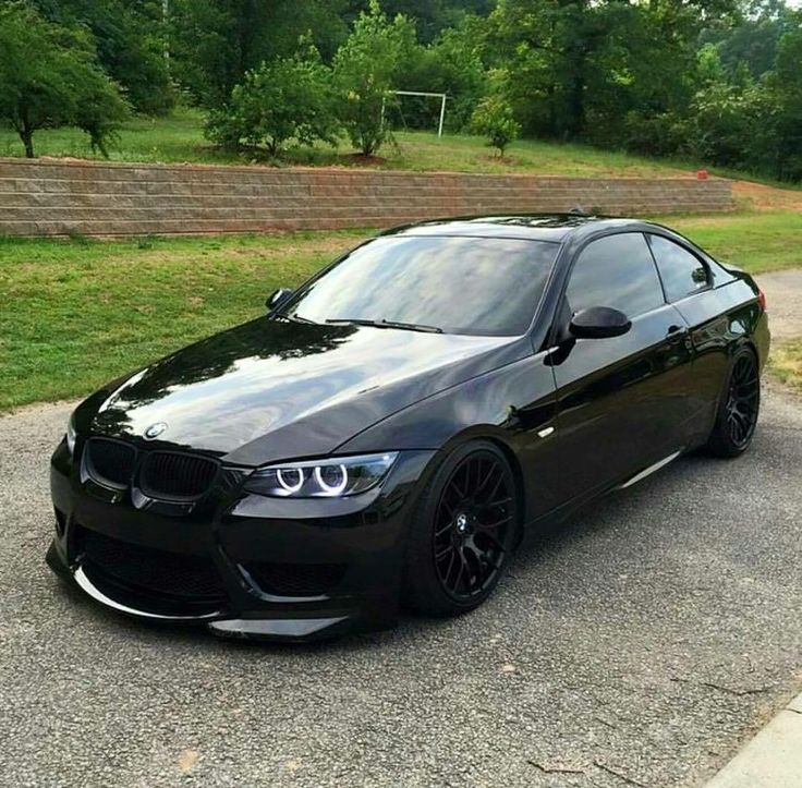 a black car parked on the side of a road next to some grass and trees