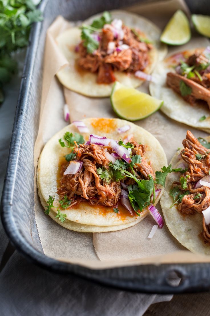 pulled pork tacos with cilantro, onions and limes on a baking sheet