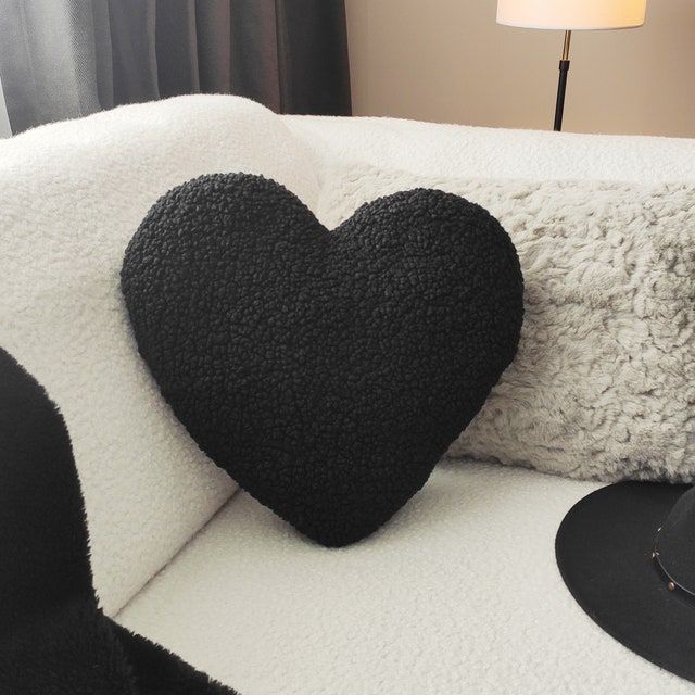 a heart shaped pillow sitting on top of a white couch next to a black hat