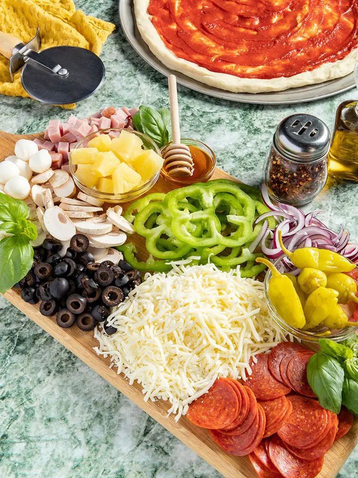 pizza ingredients laid out on a cutting board with olives, pepperoni, peppers, and cheese