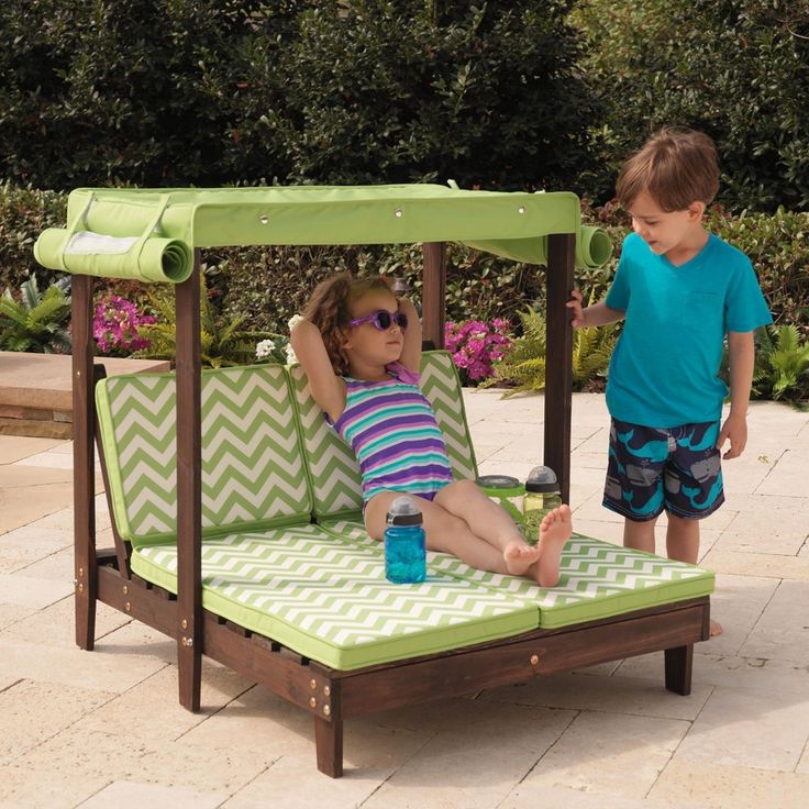 two young children playing on a green and white outdoor daybed with water bottle in it