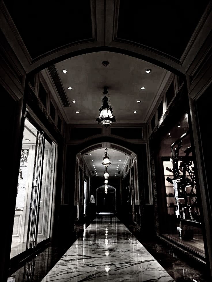 an empty hallway in a building with chandelier and lights on either side of it