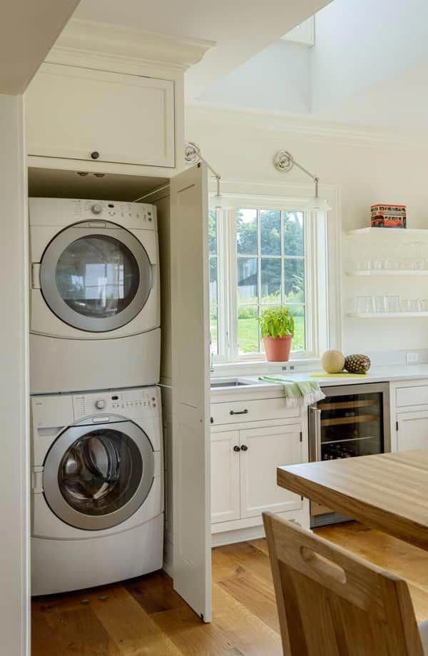 a washer and dryer in a kitchen with white cabinets, wood table and chairs