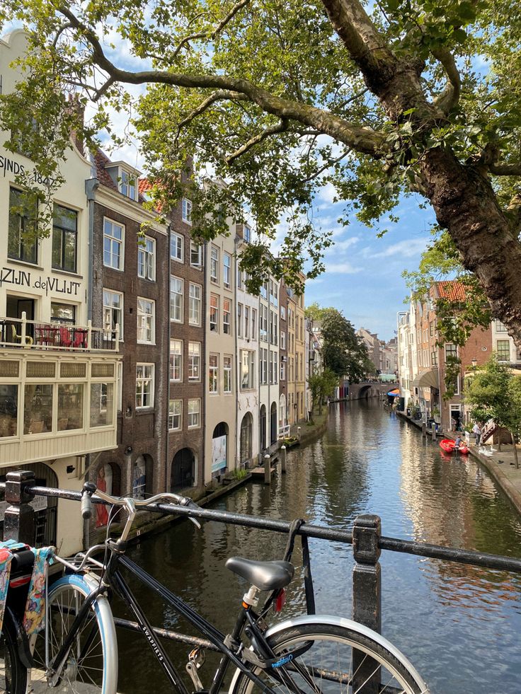 two bicycles are parked on the side of a canal in front of some buildings and trees