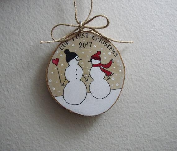 a christmas ornament with two snowmen on it hanging from a string against a white wall