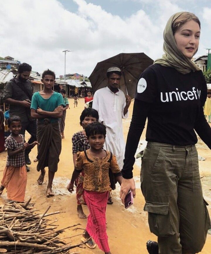 a group of people walking down a dirt road with an umbrella over their heads and one woman in the foreground