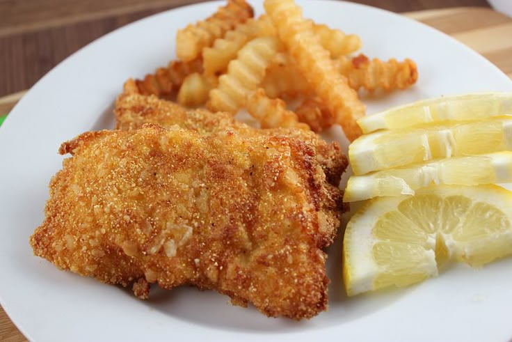 fried chicken, french fries and lemon wedges on a white plate