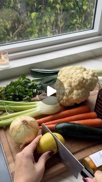 a person cutting up vegetables on top of a wooden table next to a window with a knife