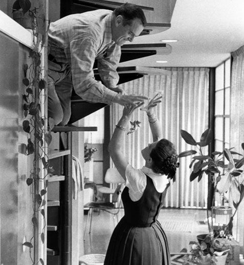 a man and woman standing on top of a stair case next to each other in a living room