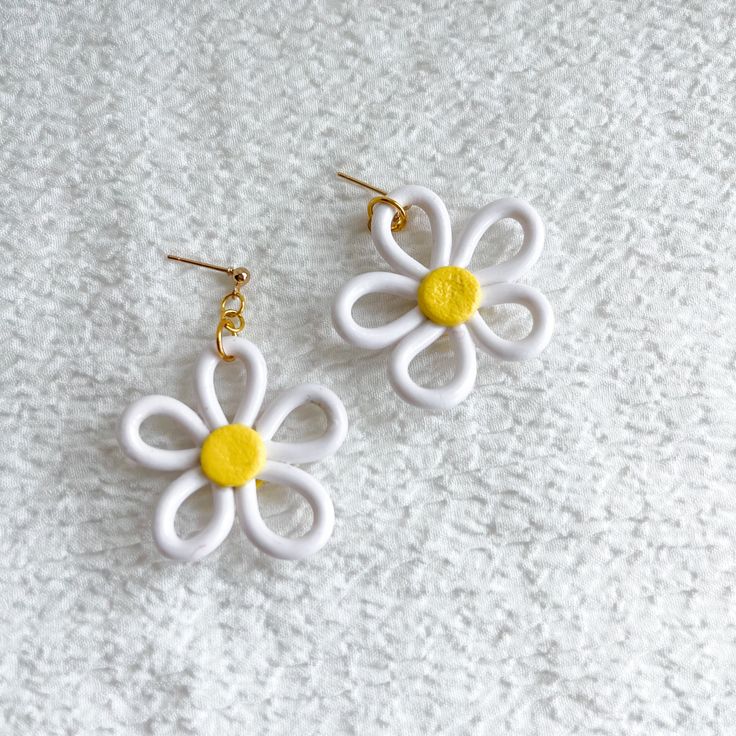 two white and yellow flower shaped earrings sitting on top of a bed next to each other