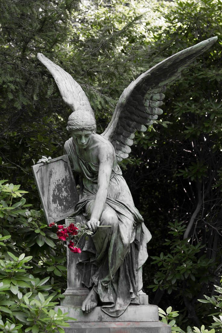 an angel statue sitting on top of a cement block in the middle of some trees