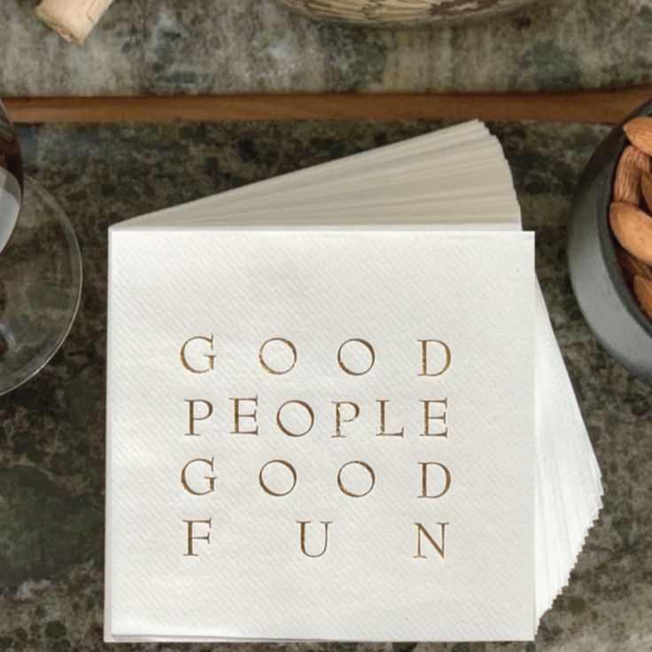 a napkin with the words good people go fun on it next to some wine glasses and nuts