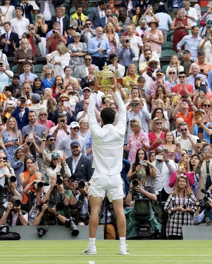 a tennis player raises his racket in the air as people watch from the stands